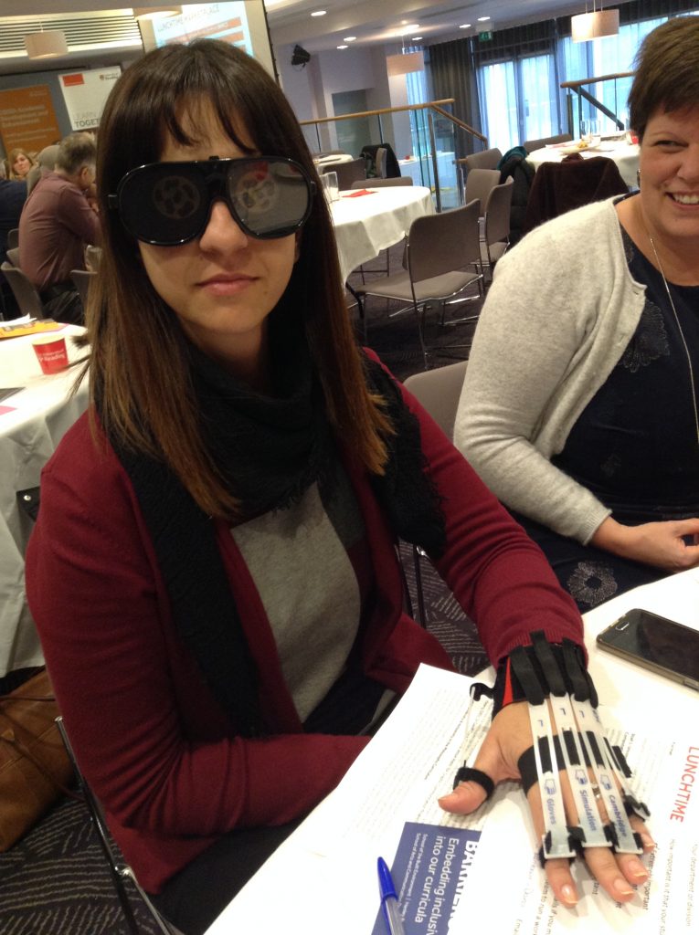 person wearing goggles simulating diabetic retinopathy and gloves to impair dexterity