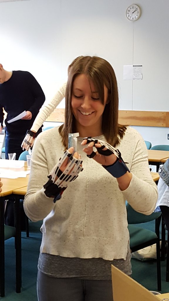 A student wearing gloves that simulate dexterity impairment trying to open a small sachet of thickering.