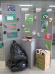 Grey display boards with posters, black sacks and post-box with big eyes on it advertising how to improve recycling efforts.