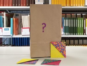 Brown paper bag with a question mark on it, and 3 origami folded bookmarks next to the bag.