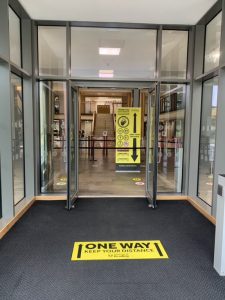 The main entrance of the Library, now featuring a bright yellow One Way sticker on the floor, pointing inside the Library to indicate that Library users should enter only at the main entrance.
