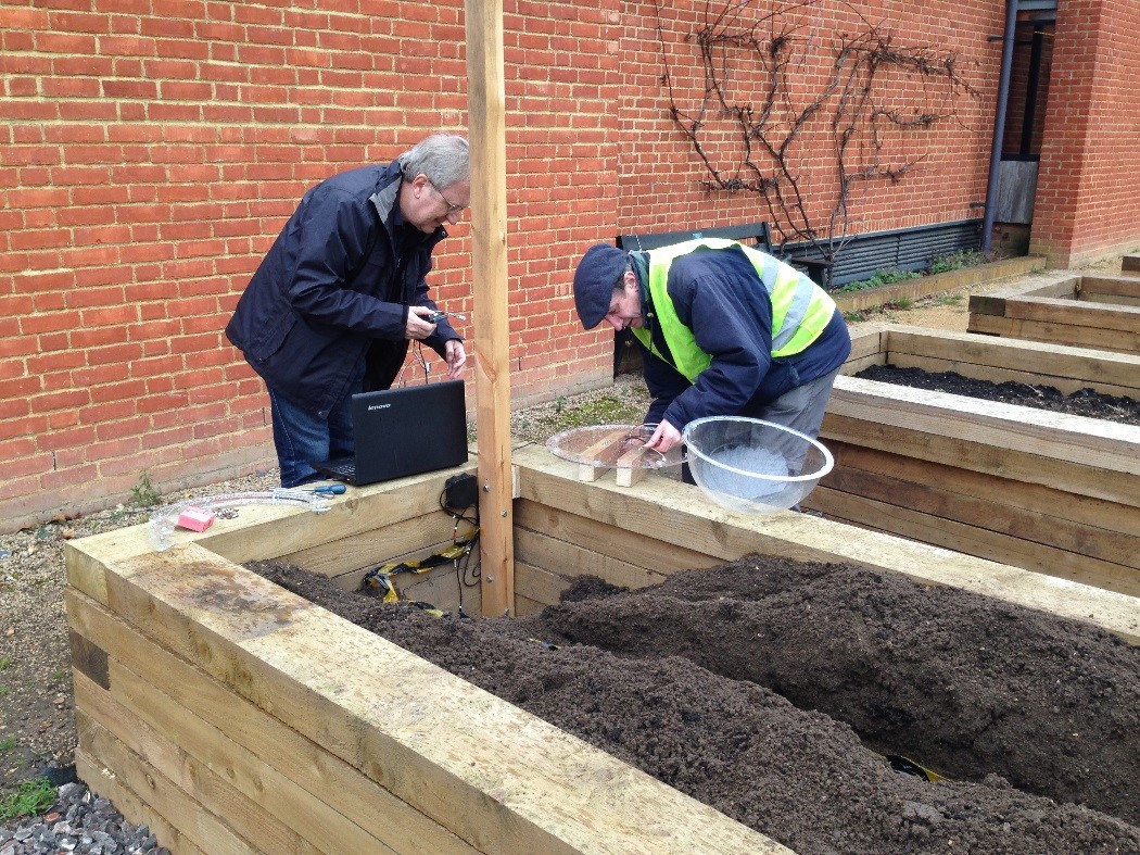 Image of Richard and Mike from Reading Hackspace installing monitoring equipment in the Beet Box garden bed.