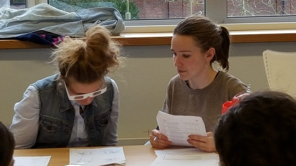 One student administers a speech and language assessment to another who is wearing vision impairment simulation glasses.