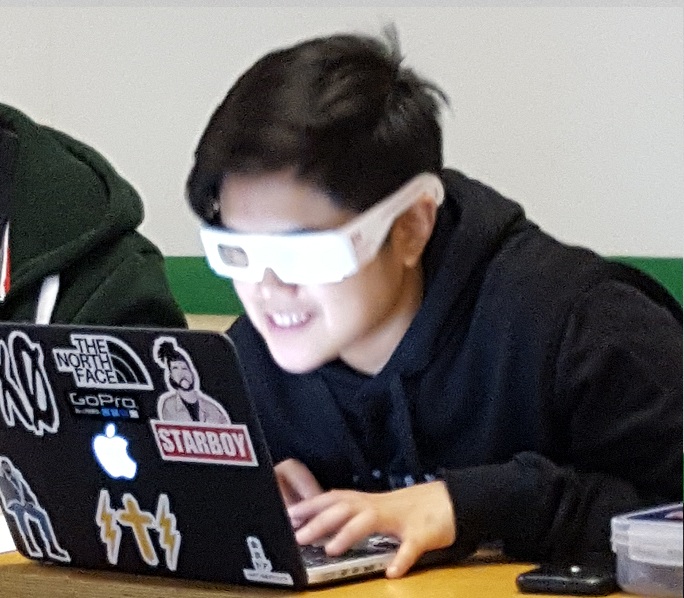 A student wearing simulator glasses interacting with a laptop.