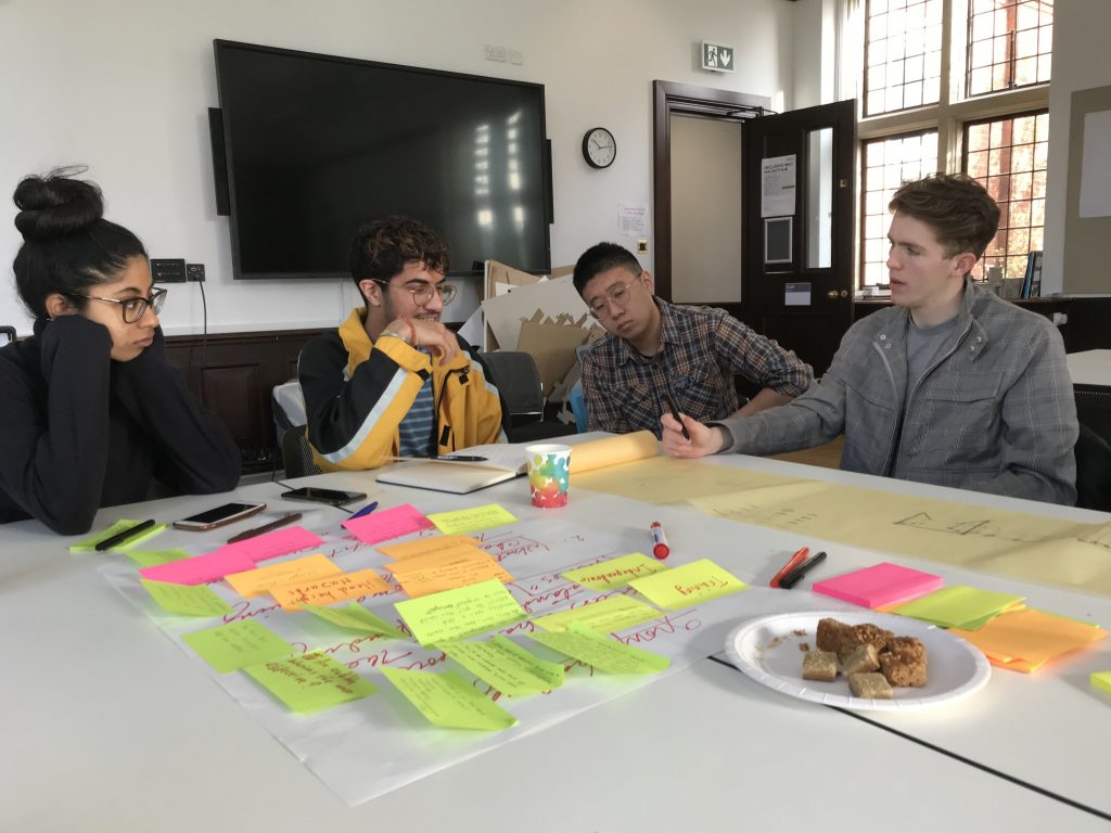 Four students sitting around a table working with sketches and post-it notes