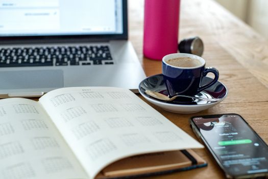 Image shows a book, a laptop and a cup of coffee