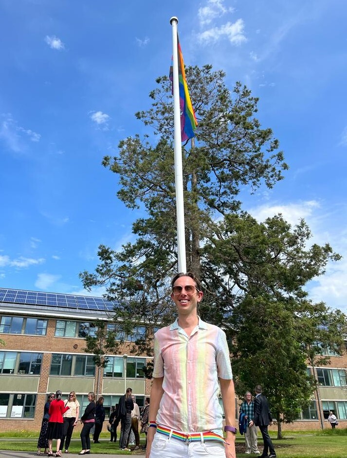 Ruvi, Chair of the LGBT+ Staff Network standing in front of the flying Pride flag on Whiteknights Campus.