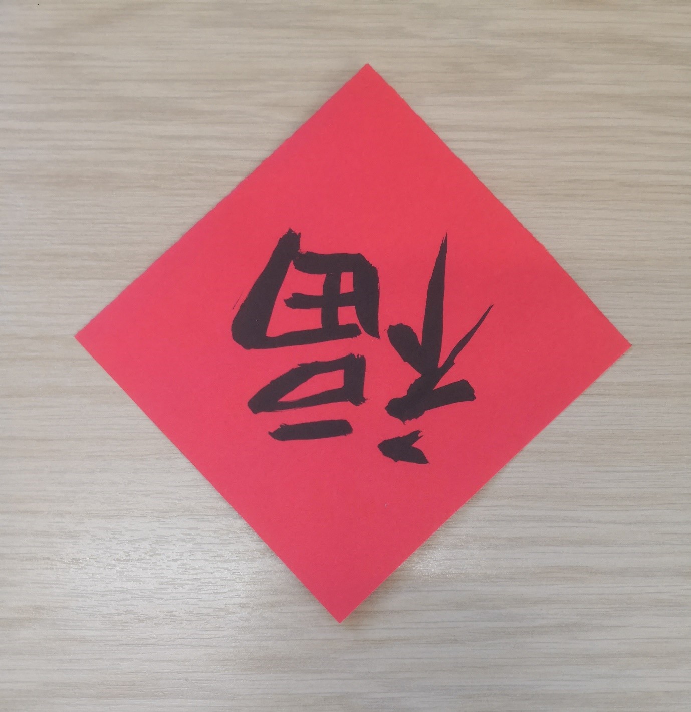 A photograph showing a square of red paper with the character "Fu" painted on in calligraphy and inverted.