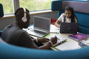 Black young man in headphones and Asian young woman seated at Library study table
