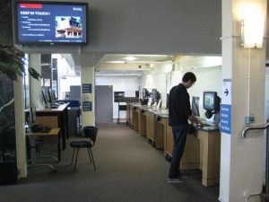 Man uses Library Self-Service Point machines of right, computers on left.