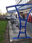 Blue bike shelter with red and white tape wrapped around it, enclosing two abandoned and unloved bikes, 