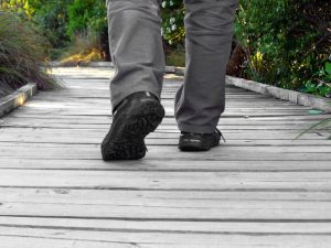 Feet in trainers and grey trousers walk on grey wooden path