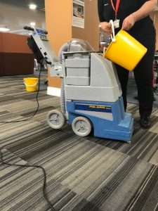 Member of staff filling carpet cleaning machine with water to wash carpets as part of the annual summer big clean