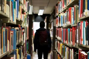 Image of person with rucksack walking through library aisle