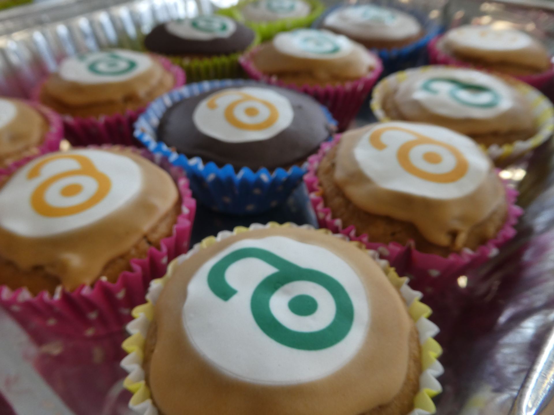 A tray of small iced cupcakes with the open access logo in green or gold on top 