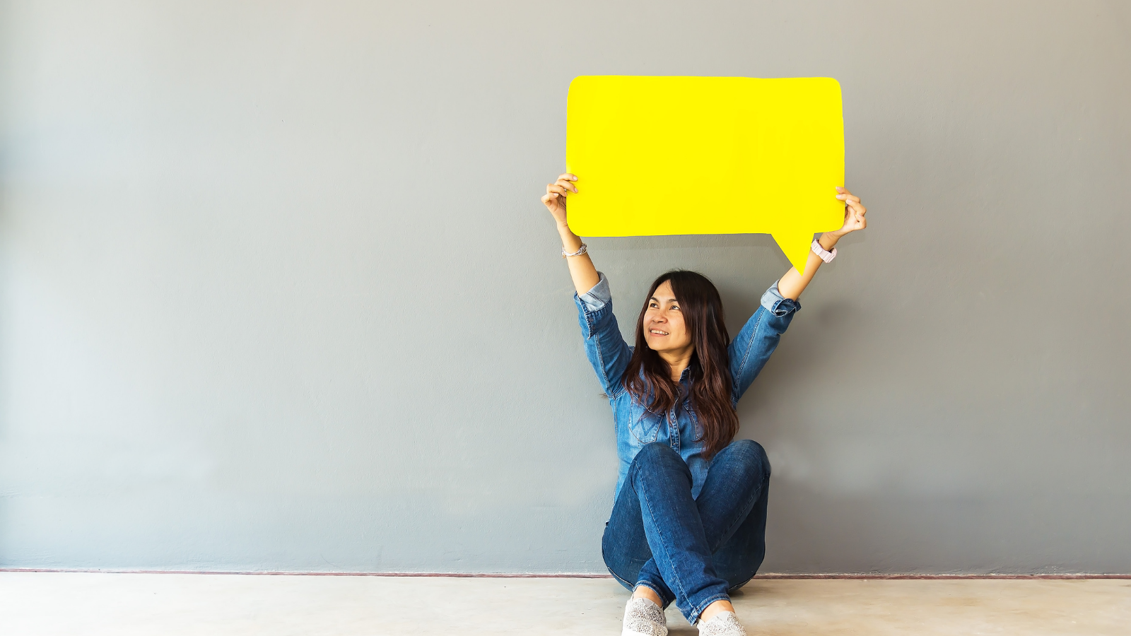Image of a girl sitting on the floor holding up a yellow speech bubble