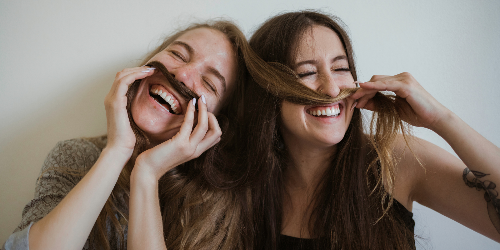 Two girls laughing, they are playing around with hair to make mustaches