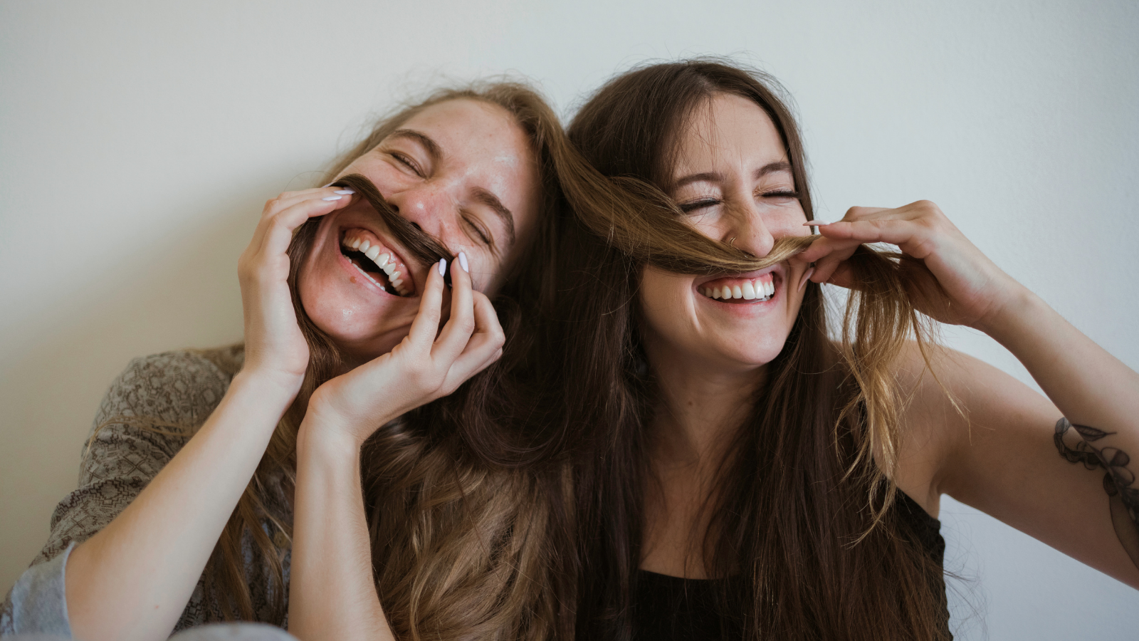 Two girls laughing, they are playing around with hair to make mustaches