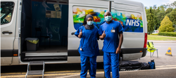 Two NHS healthcare workers standing in front of the NHS Health on the Move vaccine bus.