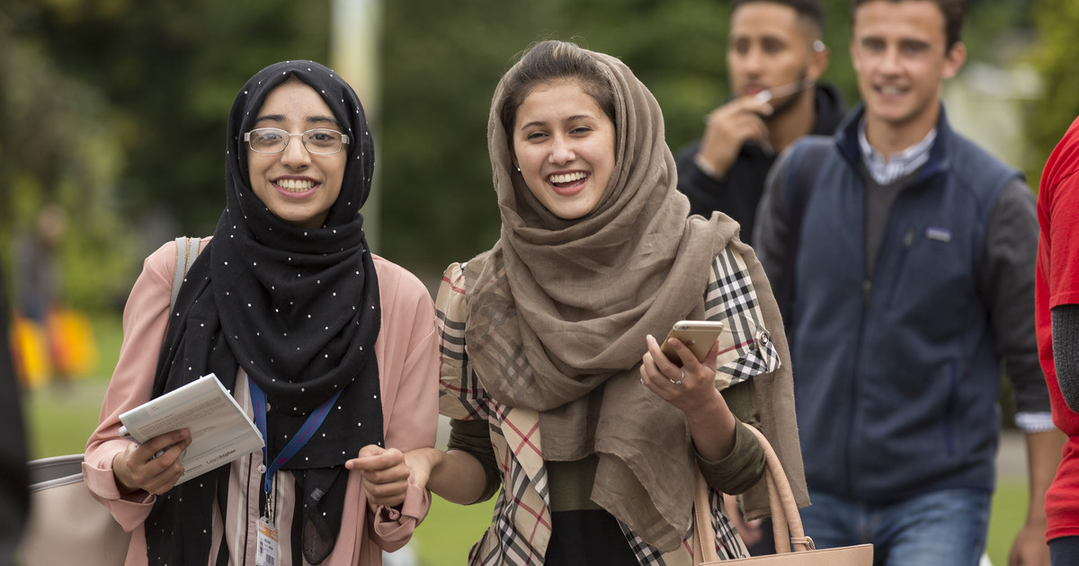 Two female students smiling on campus. They are wearing headscarves