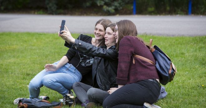 three students taking pictures in a field