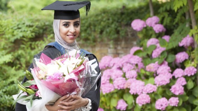A graduate holding a bouquet of flowers on the grounds of the University's London Road Campus