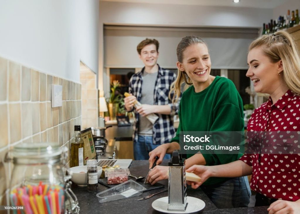 Three people in a kitchen, preparing food, laughing and chatting